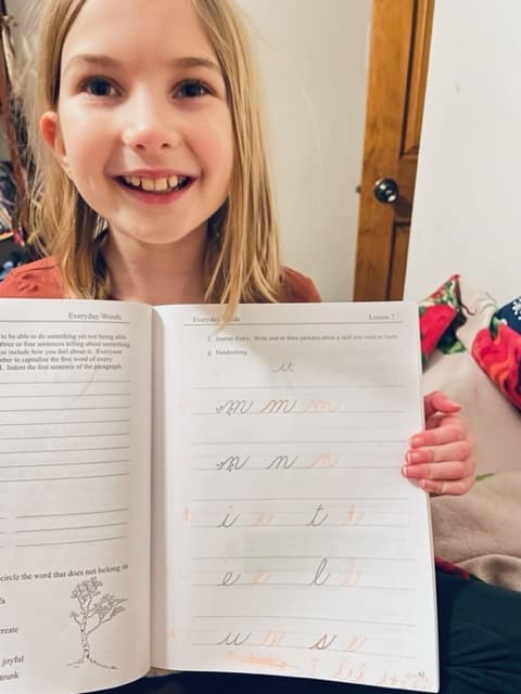 Language Arts Homeschool Curriculum - happy girl with book open to copy work