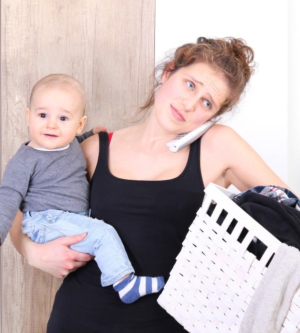 overwhelmed mama on the phone, holding laundry in one arm and child in the other